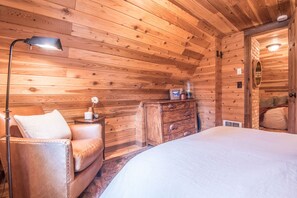 A wooden cabin bedroom with a bed, a nightstand, a dresser, and a lamp. - Wee Cottage- Unparalleled Charm, Tiny House, Enchanting Setting, Hot Tub (Sundance)
