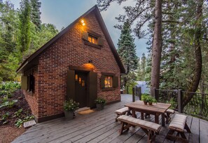 A rustic cabin with a brick exterior, a wooden deck, and a small porch area. - Wee Cottage- Unparalleled Charm, Tiny House, Enchanting Setting, Hot Tub (Sundance)