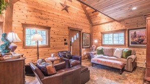 A log cabin interior with a leather sofa, a patterned rug, and wooden walls. - Wee Cottage- Unparalleled Charm, Tiny House, Enchanting Setting, Hot Tub (Sundance)