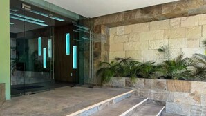 A modern building entrance with a glass door, stone steps, and a stone wall with plants.