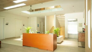 A modern reception area with a wooden reception desk, potted plants, a staircase, and a refrigerator.