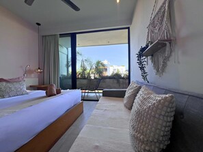 Un dormitorio moderno con una cama grande, un sofá y un balcón con vistas a edificios y árboles.
