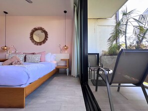 A bedroom with a bed, bedside tables, a mirror, and a view of the outdoors.