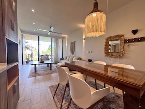 A modern dining area with a long wooden table, white chairs, and a hanging light fixture.