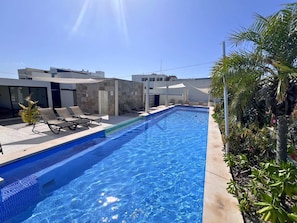 Une piscine avec des chaises longues et un bâtiment moderne en arrière-plan.