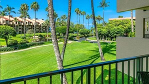 A hotel courtyard with palm trees, a well-manicured lawn, and a building with a red roof in the background.