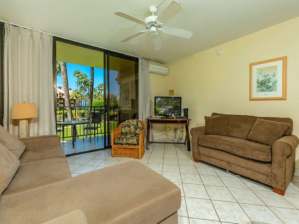 A living room with a sofa, a chair, a television, and a ceiling fan.