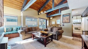 A spacious living area with a large sectional sofa, a coffee table, and a kitchen area with modern appliances. - Secluded Cozy Cabin, Forest Setting, 1-Car Garage, Near Winter Shuttle (Mammoth Lakes)