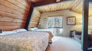 A cozy bedroom with two beds, wooden walls, a window with a view of trees, and framed pictures on the wall. - Secluded Cozy Cabin, Forest Setting, 1-Car Garage, Near Winter Shuttle (Mammoth Lakes)