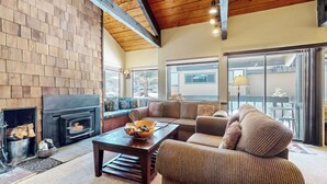A cozy living room with a fireplace, a sofa set, and a view through large windows. - Secluded Cozy Cabin, Forest Setting, 1-Car Garage, Near Winter Shuttle (Mammoth Lakes)