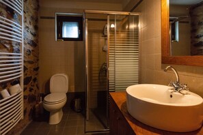 A bathroom with a white toilet, a glass-enclosed shower, and a large sink with a mirror above it. - Mystras Village House (Sparta)