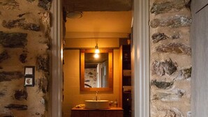 A narrow stone-walled hallway leading to a bathroom with a sink and mirror. - Mystras Village House (Sparta)