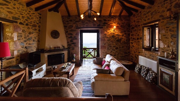 A cozy stone-floored living room with a wooden ceiling, a fireplace, a television, and a sofa. - Mystras Village House (Sparta)