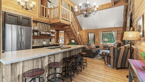 L’intérieur d’un chalet rustique comprend une cuisine, un coin repas et un escalier menant à un niveau supérieur.