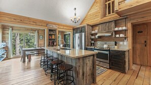 Une cuisine rustique aux murs en bois, avec un îlot central doté de tabourets de bar, un réfrigérateur, une cuisinière et un lustre.
