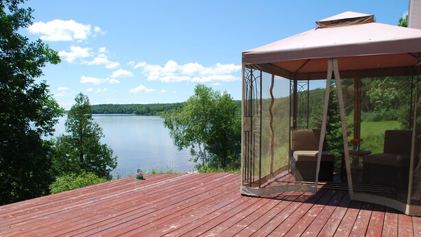Une terrasse en bois avec un espace salon couvert donnant sur un lac.