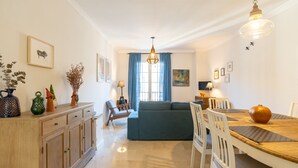 Uma sala de estar moderna com sofá, mesa de jantar, cadeiras, um armário de madeira e um candelabro.