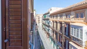 Uma rua estreita com edifícios altos, varandas e céu claro.