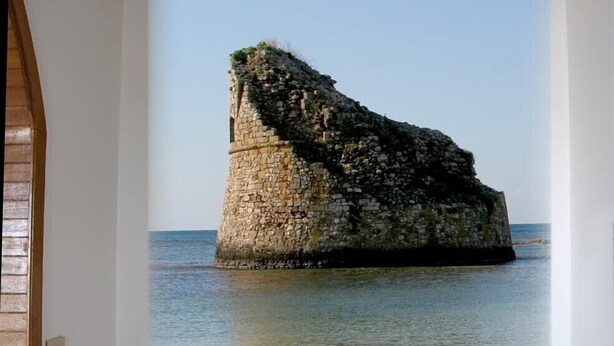 Una habitación con un amplio ventanal que muestra una escena costera con una estructura de piedra en el agua.
