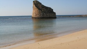 Una gran formación rocosa aislada en el mar, con una playa arenosa al frente.