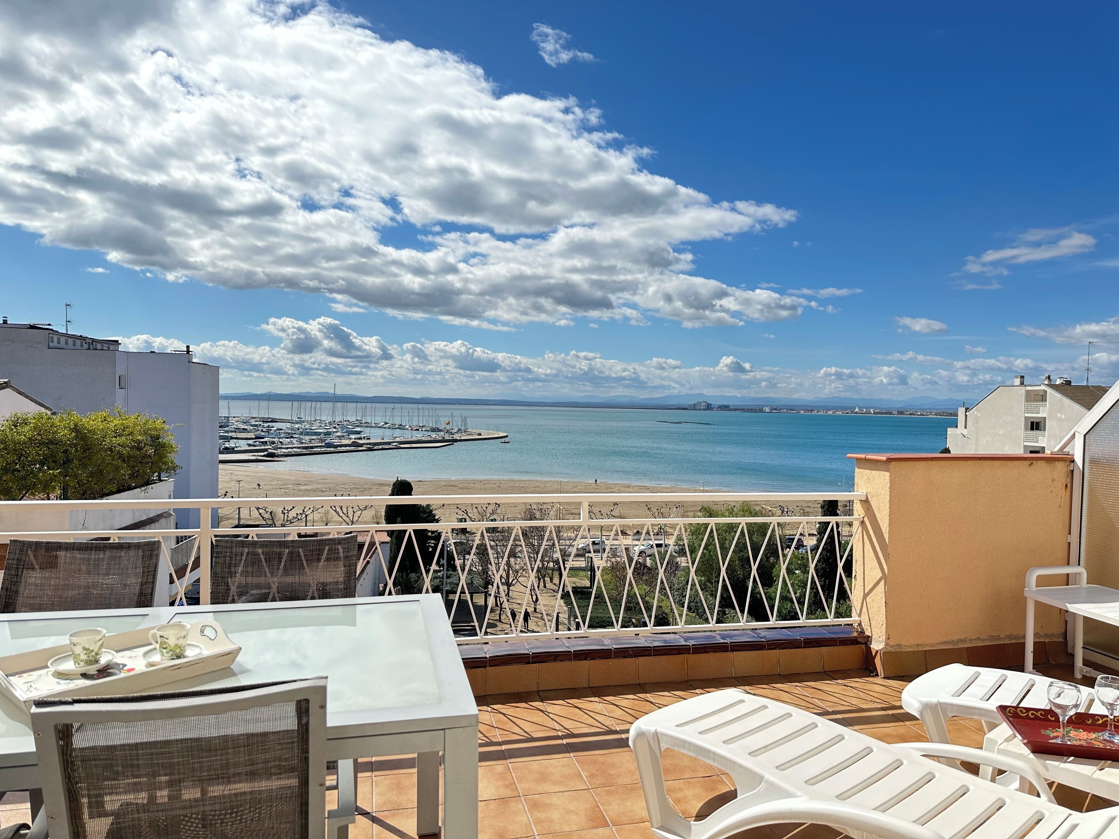 Une terrasse avec une table et des chaises, donnant sur une marina et une plage.