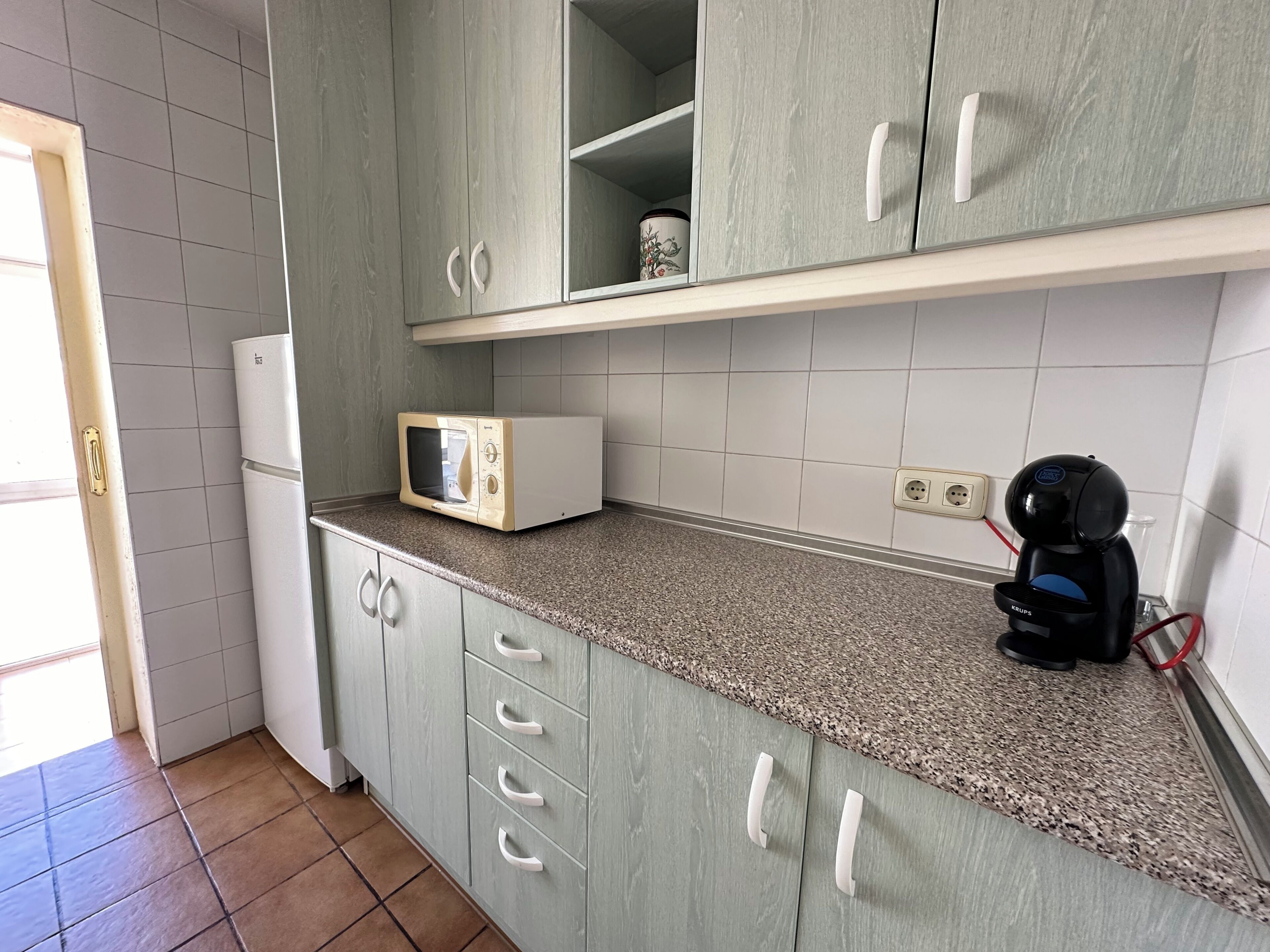 Una cocina con gabinetes grises, un microondas, una cafetera y un refrigerador.