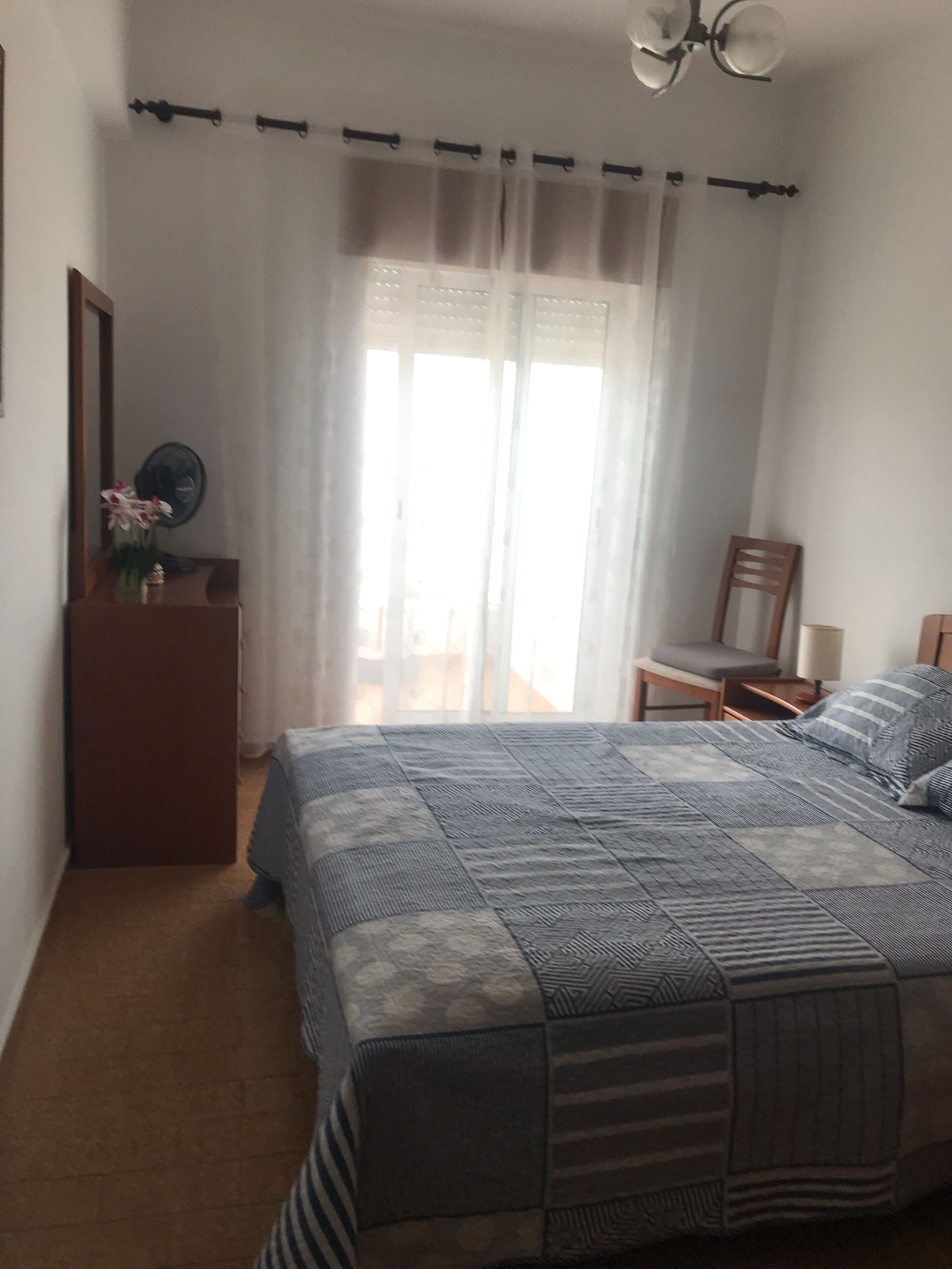 A bedroom with a bed, a chair, a desk, and a window with curtains.