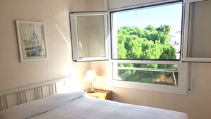 Un cuarto de hotel con una cama, un ventanal con vista a vegetación, una lámpara y un cuadro en la pared.