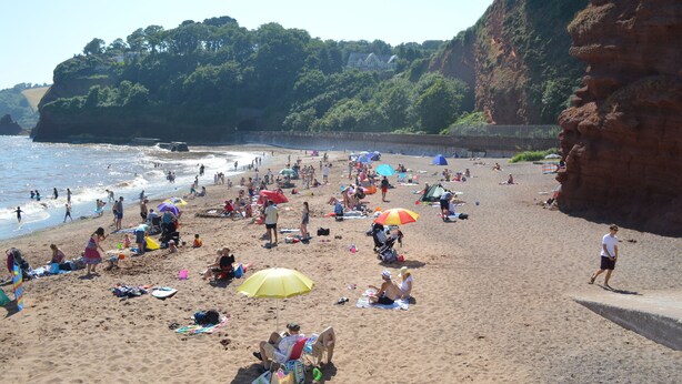 Una playa concurrida, gente tomando el sol y paseando por la orilla.