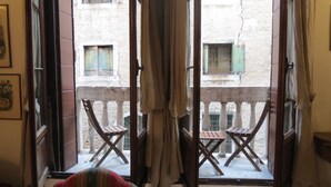 A room with a balcony, wooden chairs, and a view of a building with a stone facade. - A magnificent XVth Century gothic Noble Palace on two canals. (Venezia)