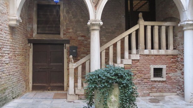 A historic building with a wooden door, a stone staircase, and a decorative urn. - A magnificent XVth Century gothic Noble Palace on two canals. (Venezia)