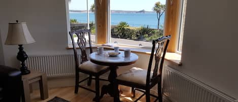 A dining area with a table and chairs, a lamp, and a view of the sea through large windows.