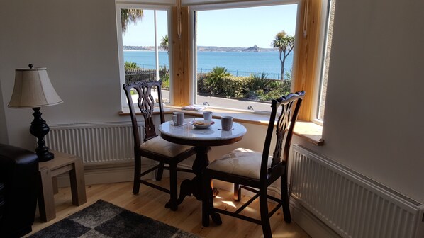 Un comedor con una mesa y sillas, una lámpara y vistas al mar a través de amplios ventanales.