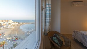 A room with a view of a beach, a wicker chair, a bed, and an air conditioning unit. - ATLANTICO Family Home by Cadiz4Rentals (Cádiz)