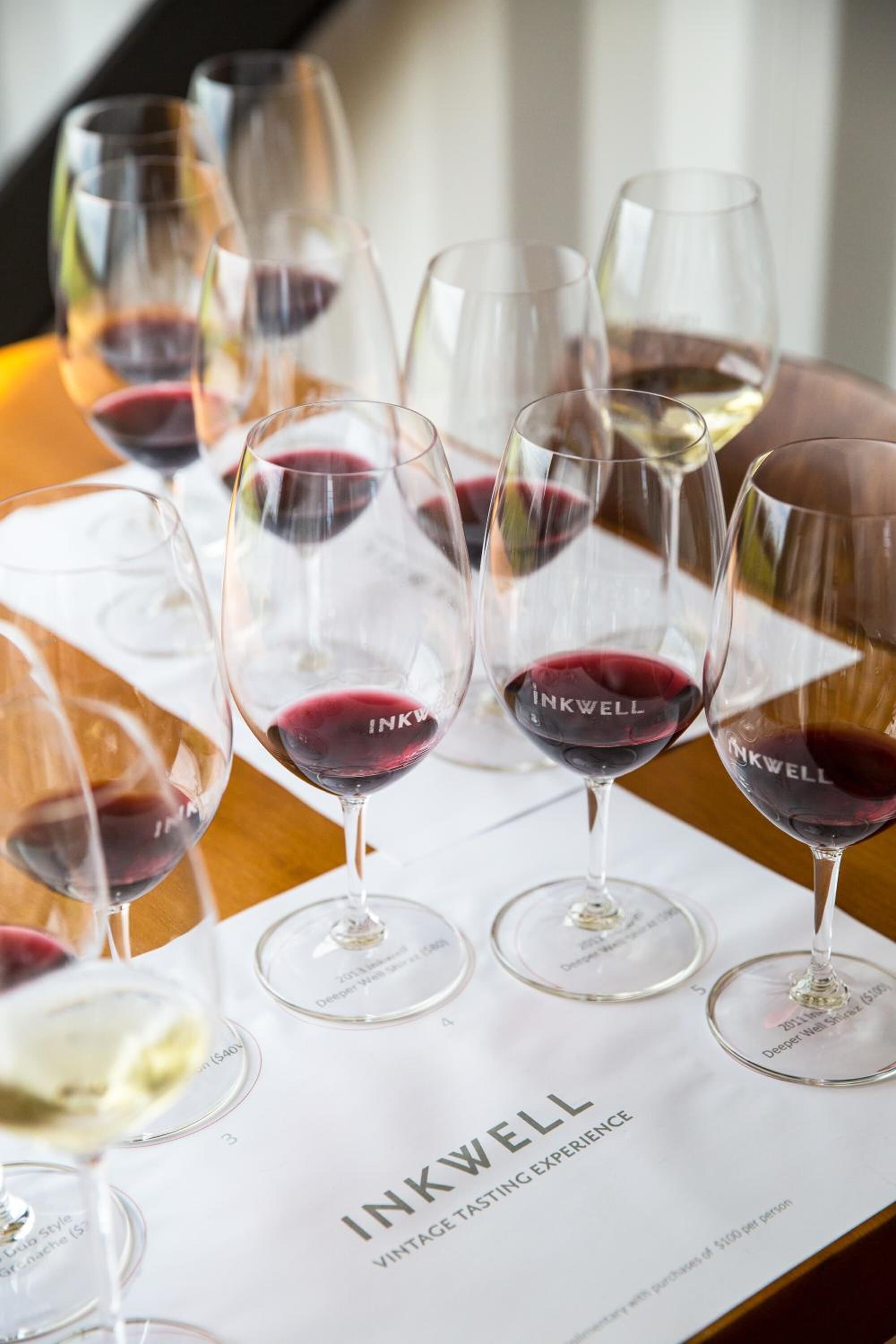 Wine glasses on a table with a menu titled "INKWELL Vintage Tasting Experience".