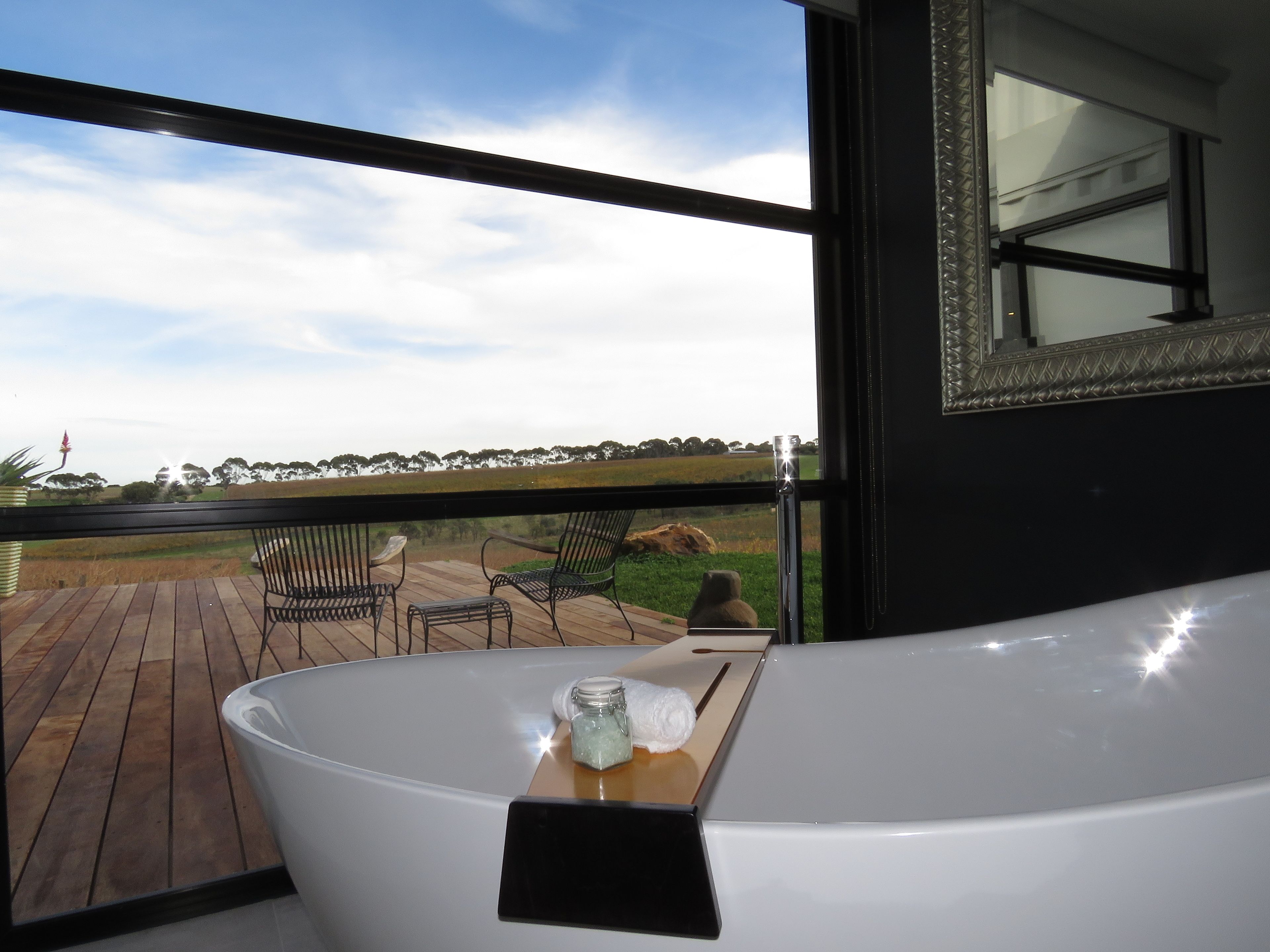 Un baño moderno con una bañera grande, terraza de madera, asientos al aire libre y vistas al campo.