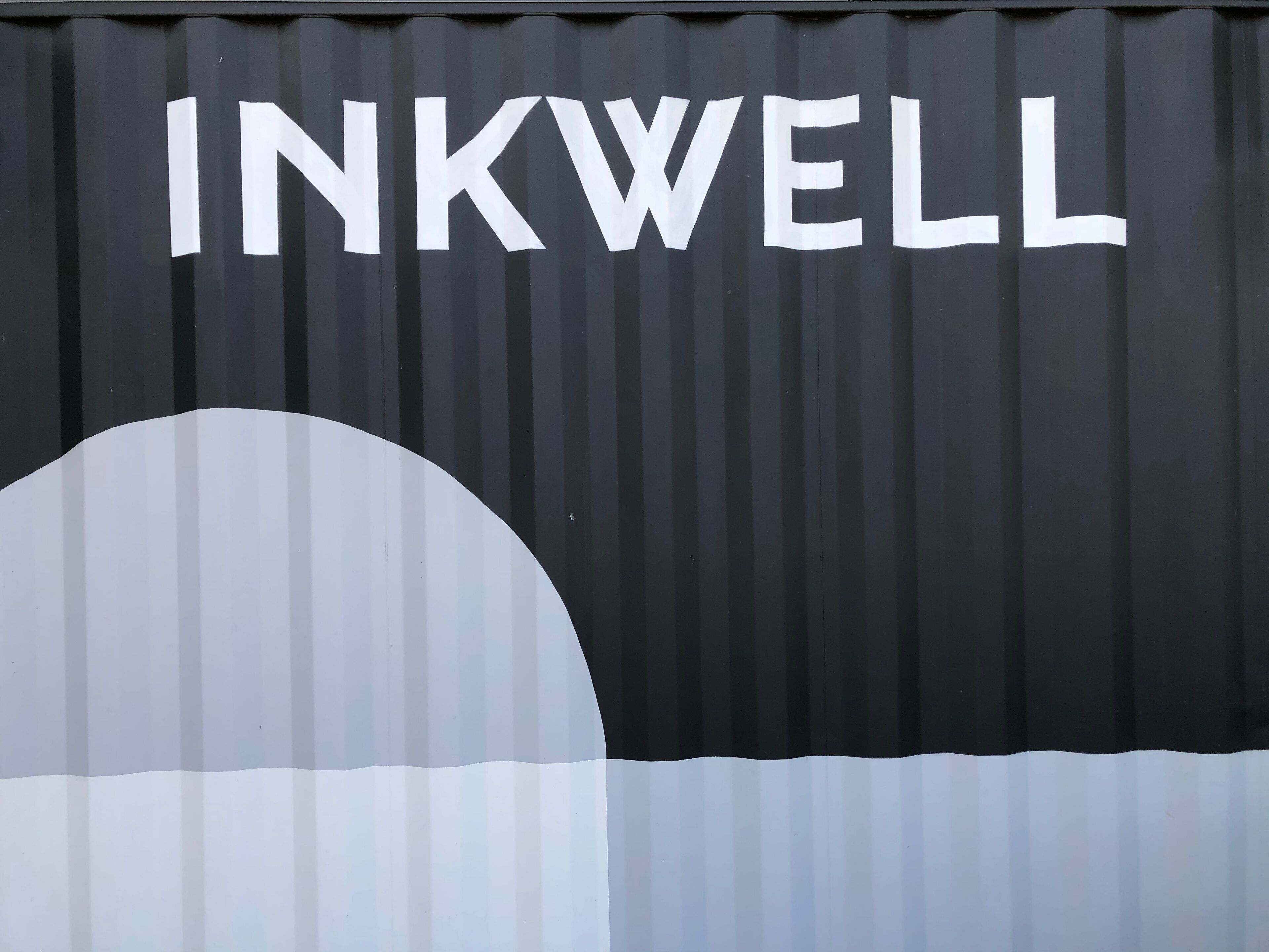 A black corrugated metal wall with the word "INKWELL" painted in white letters.