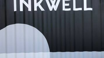 A black corrugated metal wall with the word "INKWELL" painted in white letters.