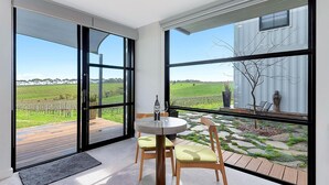 A modern room with large windows, a round table with chairs, and a view of a vineyard. - Hotel California Road at Inkwell Wines (Tatachilla)