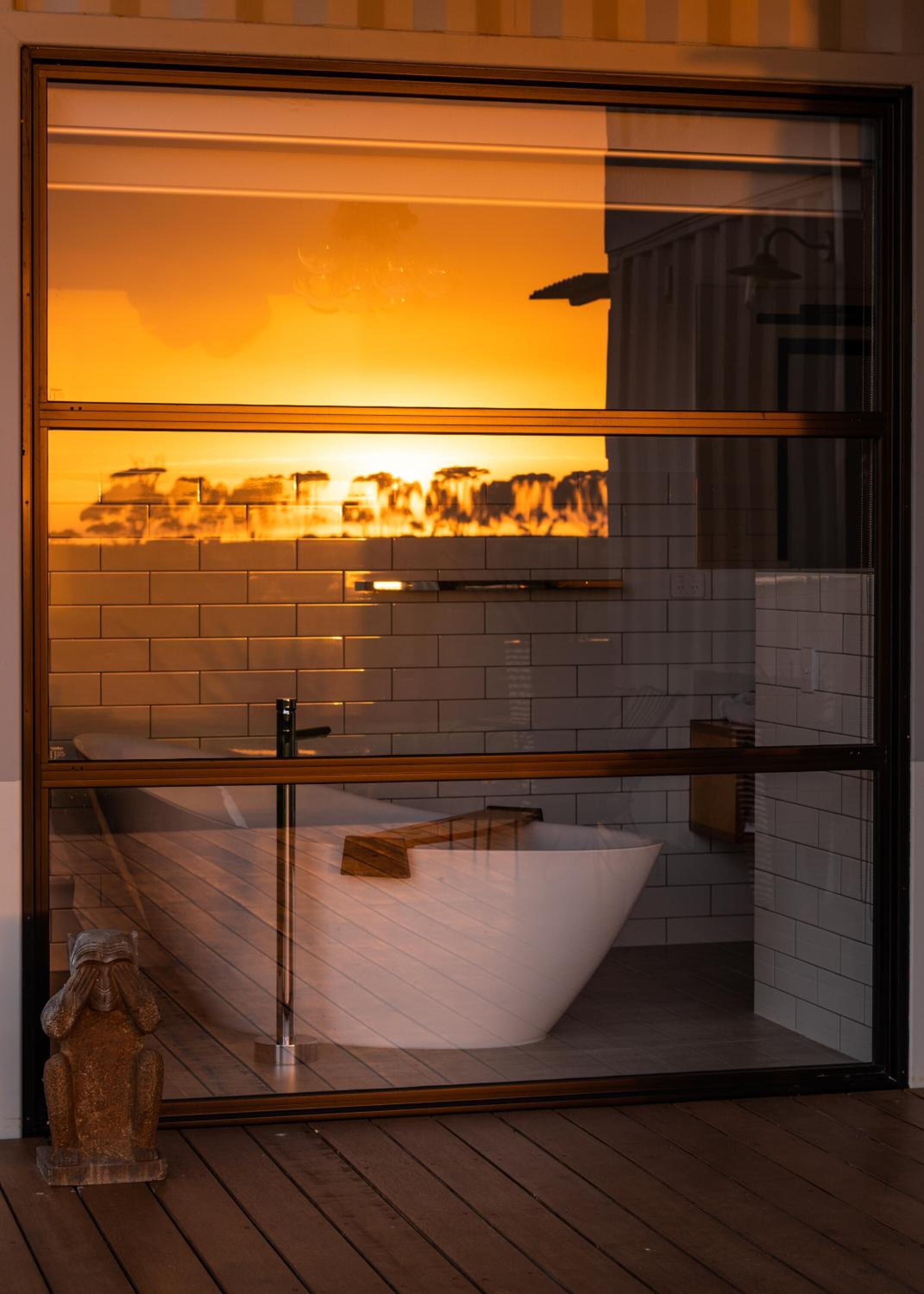 Un baño moderno con una bañera independiente, cabina de vidrio y vistas a un paisaje urbano al atardecer.