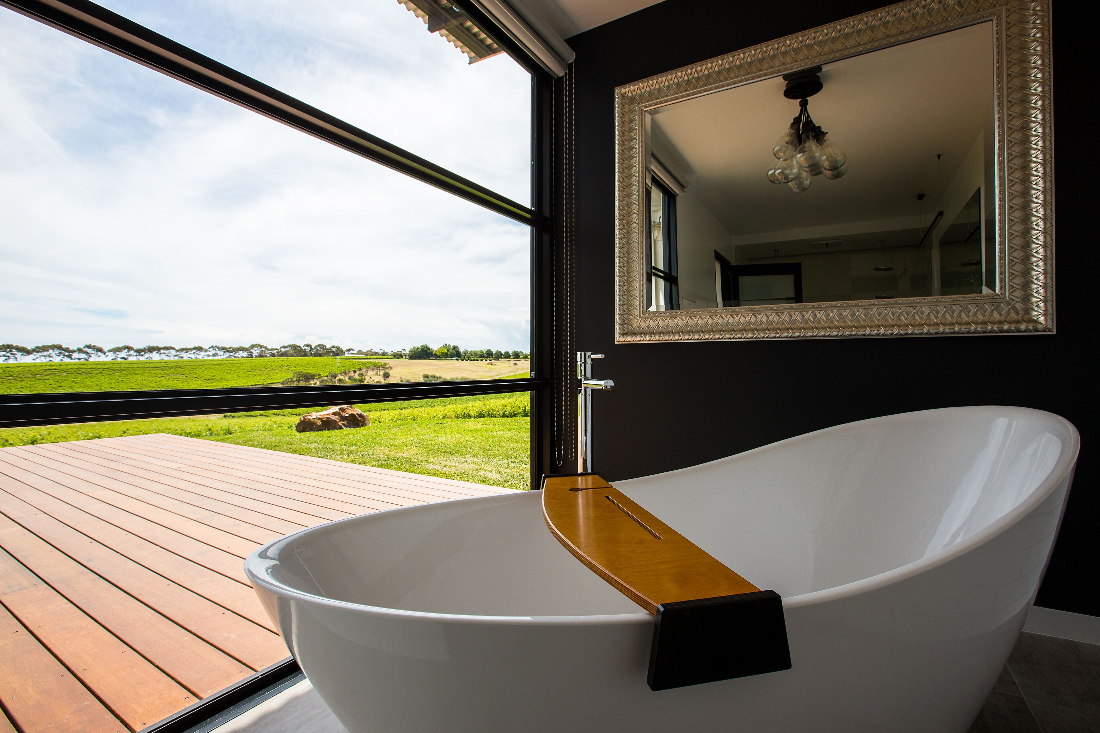 Een moderne badkamer met een vrijstaand bad, een grote spiegel en uitzicht op een groen landschap door een open deur.