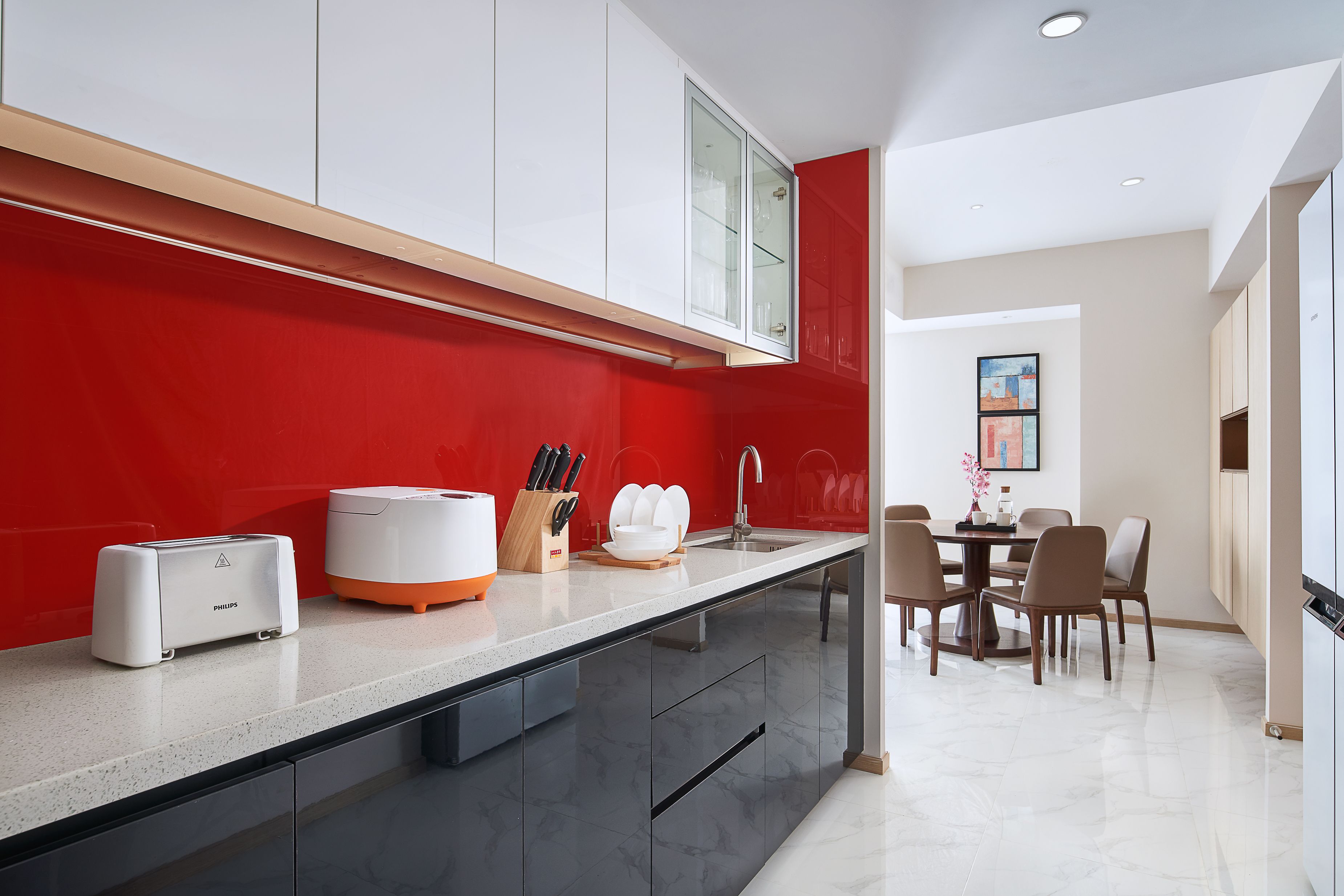 A modern kitchen with a red accent wall, a built-in island, and a dining area with a table and chairs.