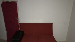 A small, single-bed room with a red bedspread, a black nightstand, and a red curtain.