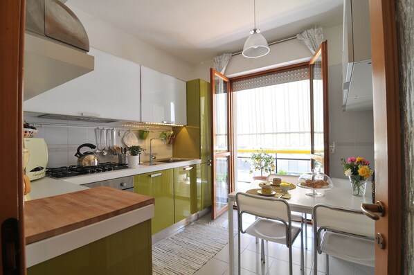 A modern kitchen with a wooden countertop, a dining area with a table and chairs, and a view of the outdoors through a window.