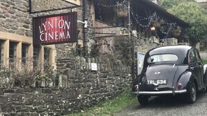 En gammal bil parkerad framför en byggnad med en skylt som visar texten ”LYNTON CINEMA”.