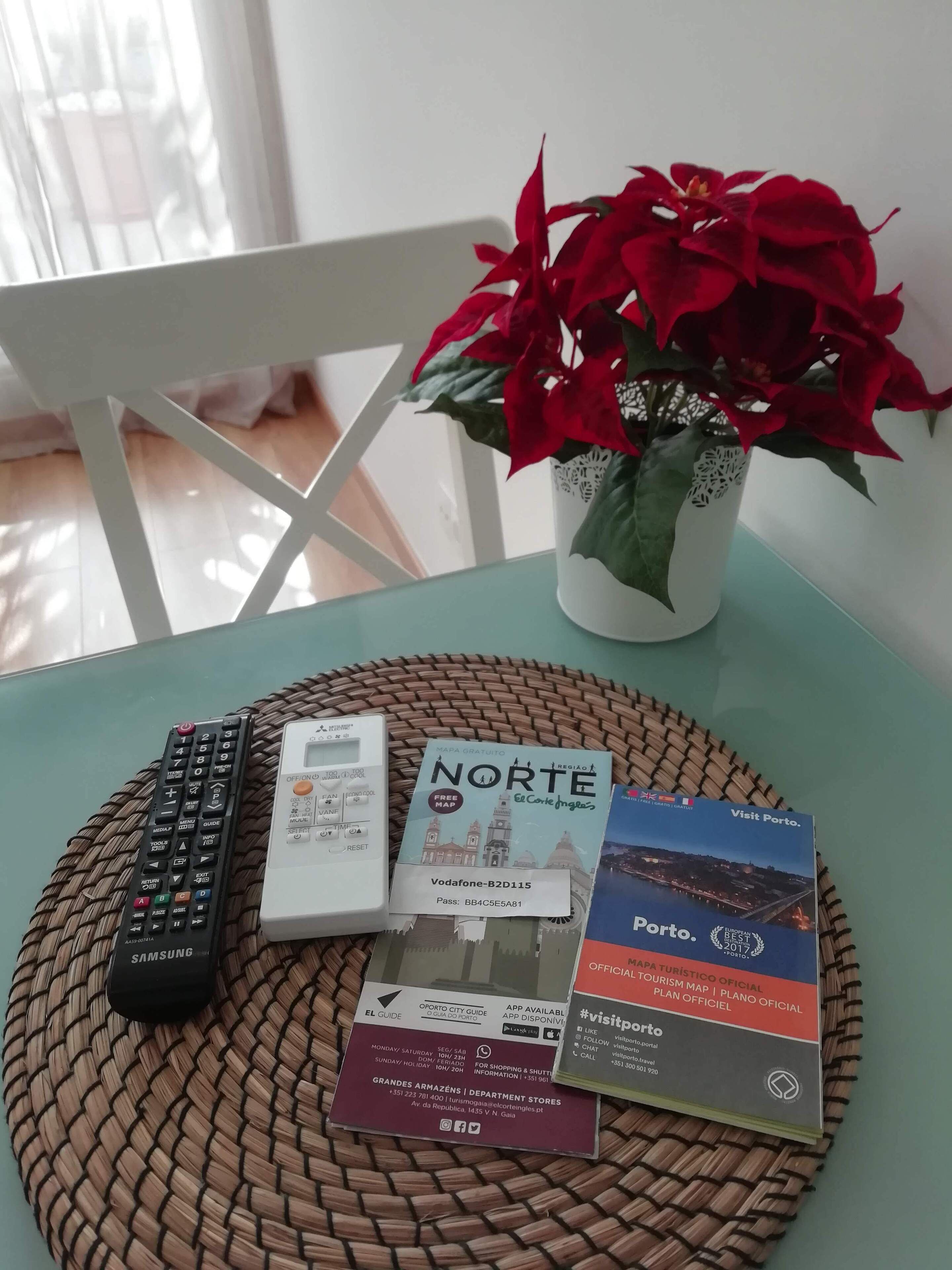 A table with a woven placemat, a remote control, a map, a flower vase, and a booklet.