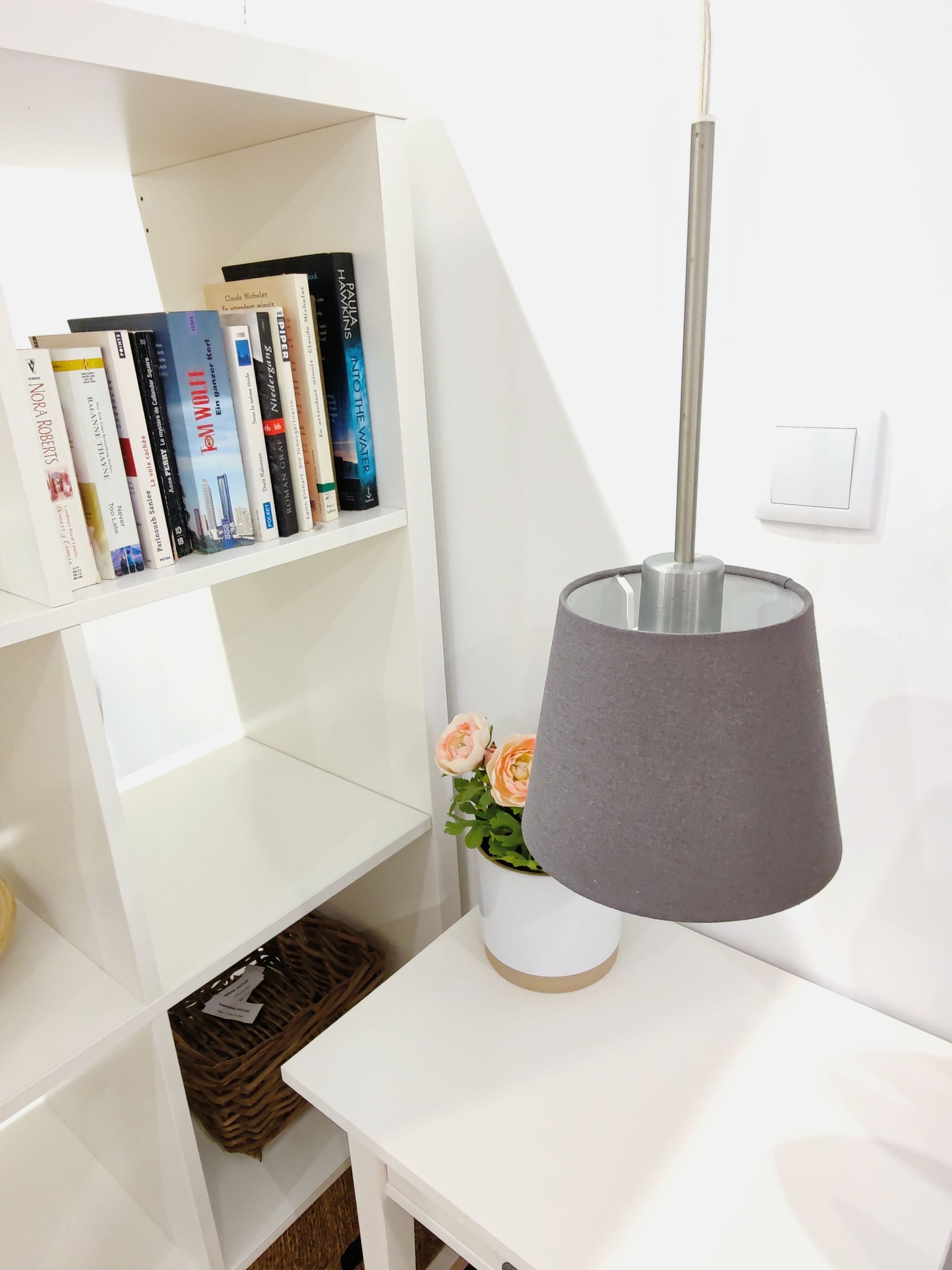 A white bookshelf with books and a small vase with flowers.