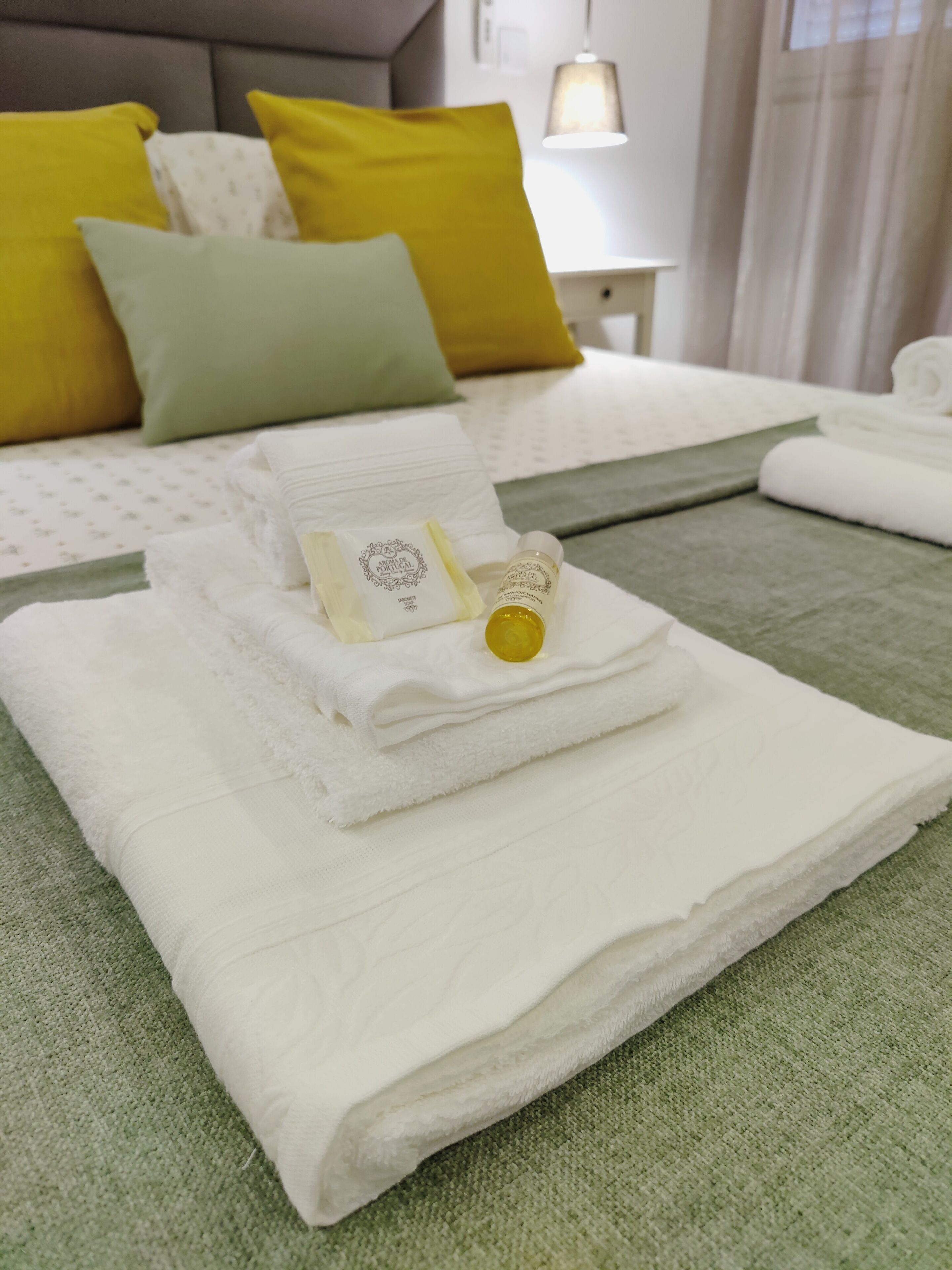 A neatly made bed with white linens, a folded towel, and a bottle of lotion.