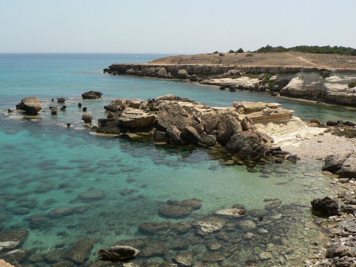 Une côte rocheuse bordée d’une eau claire et donnant sur une terre lointaine.