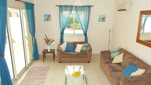 Ein Wohnzimmer mit einem braunen Sofa, einem Glastisch und einem blauen Vorhang.